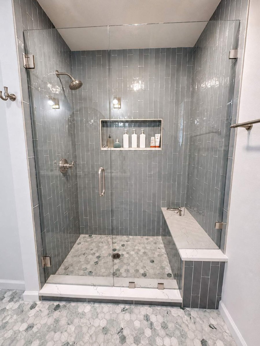 Gray glass tile shower with brass fixtures, niche, and quartz bench