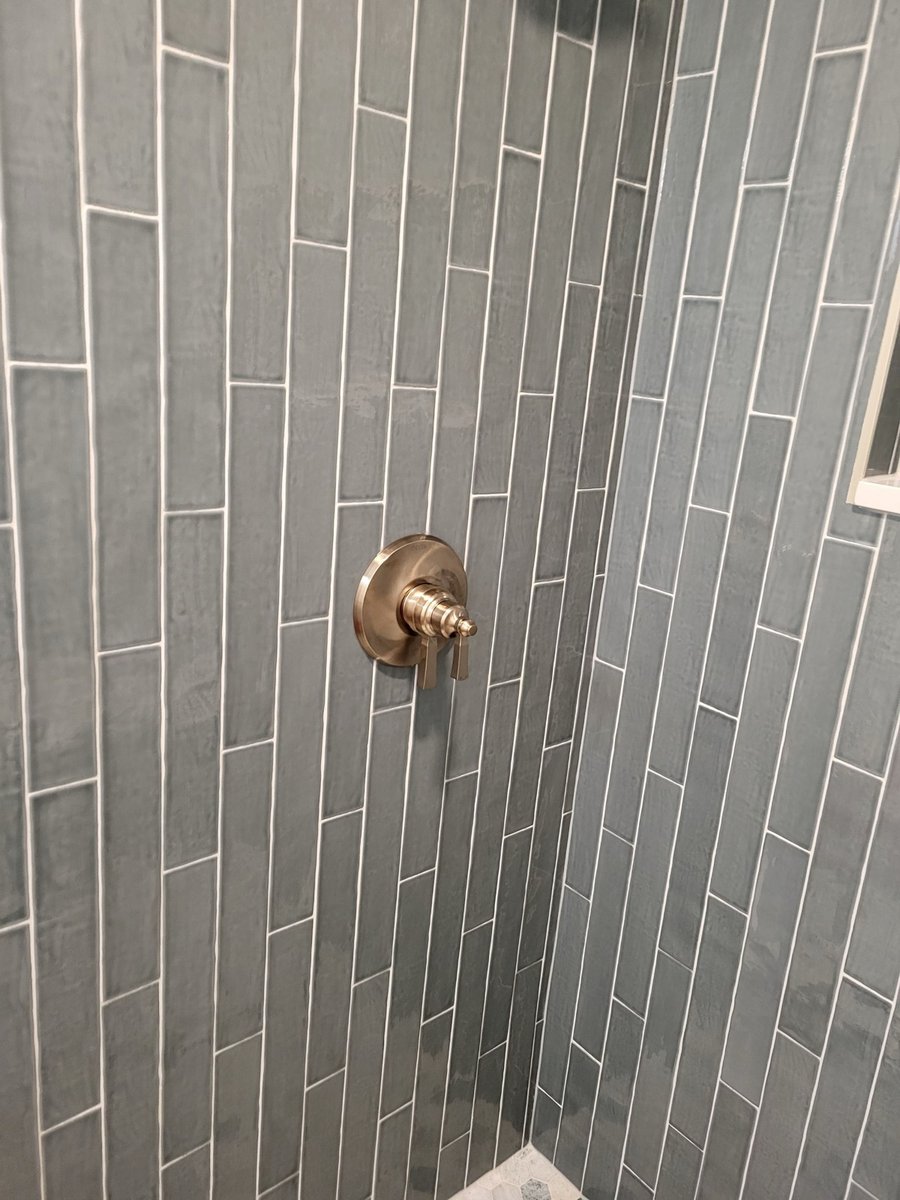 Gray subway tile shower with brass fixtures and hexagon mosaic floor