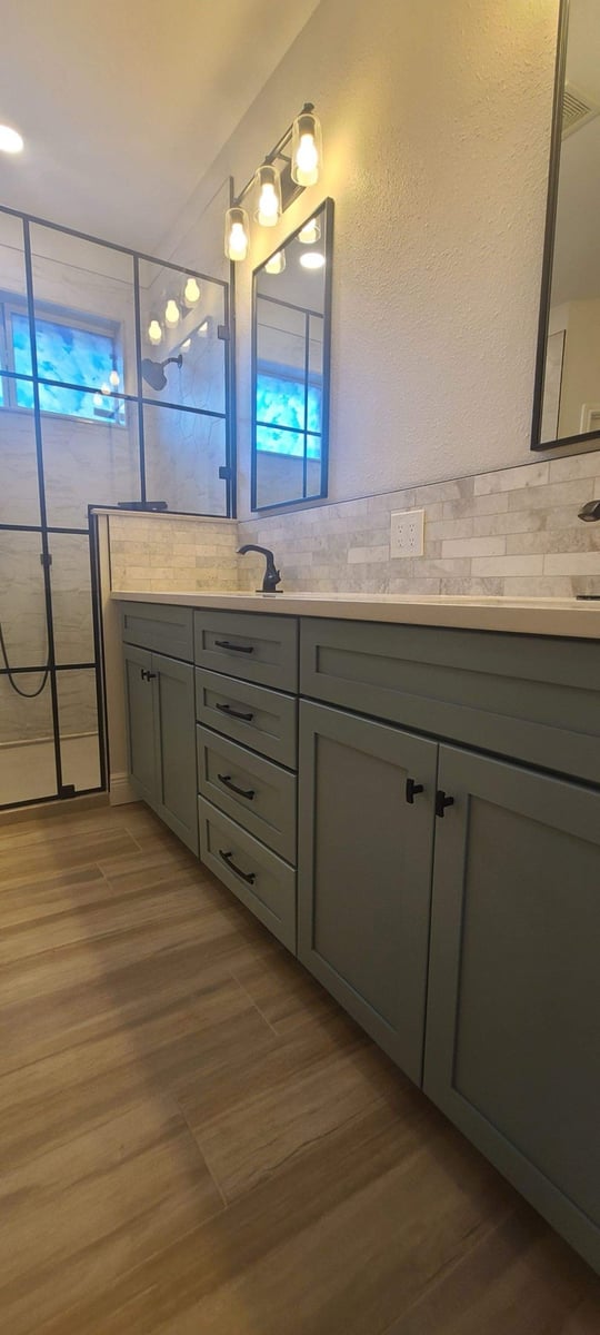 Bathroom vanity with sage green cabinets, marble subway backsplash, and black mirrors