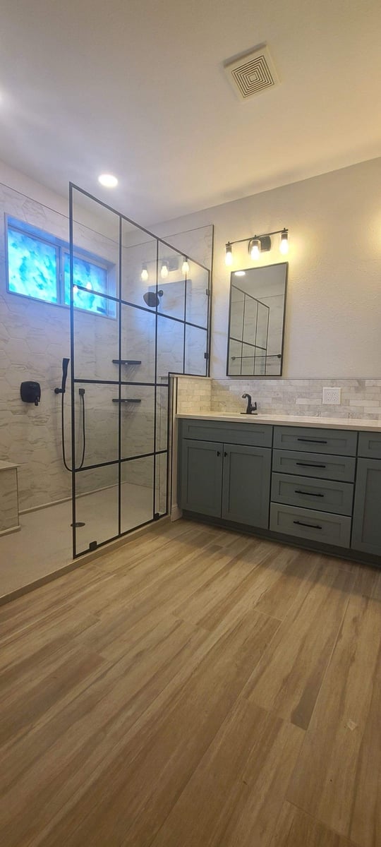 Wood-look tile bathroom with framed glass shower and sage green vanity