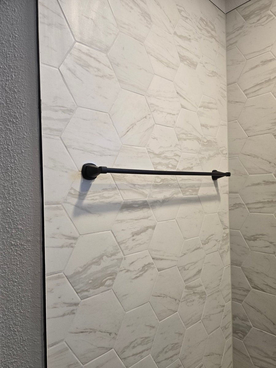 Black towel bar mounted on white marble hexagon tile wall