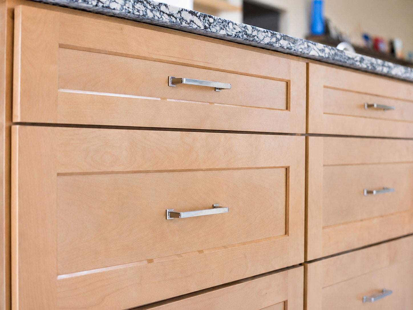 Close-up of natural wood kitchen island drawers with sleek metal pulls and patterned stone countertop.