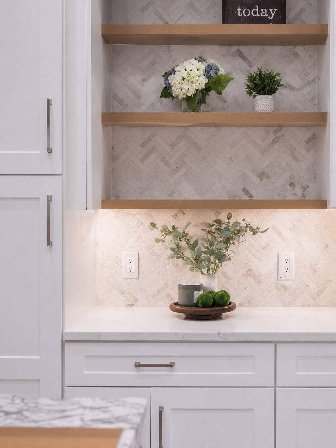 White kitchen hutch with wood floating shelves, herringbone tile, and under-cabinet lighting in Deerfield.