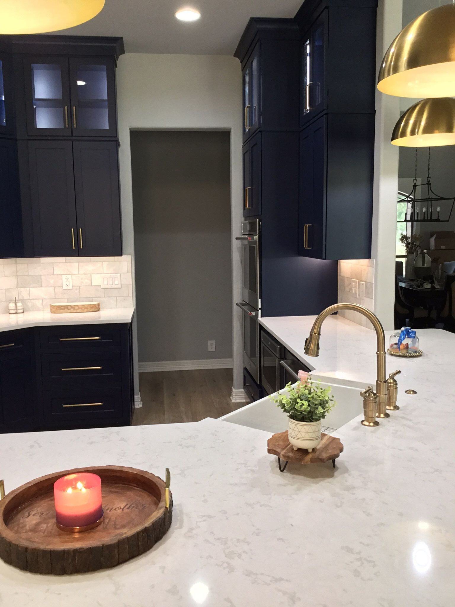 Remodeled kitchen with ample cabinets in a dark blue color, white marbled countertops, and gold fixtures