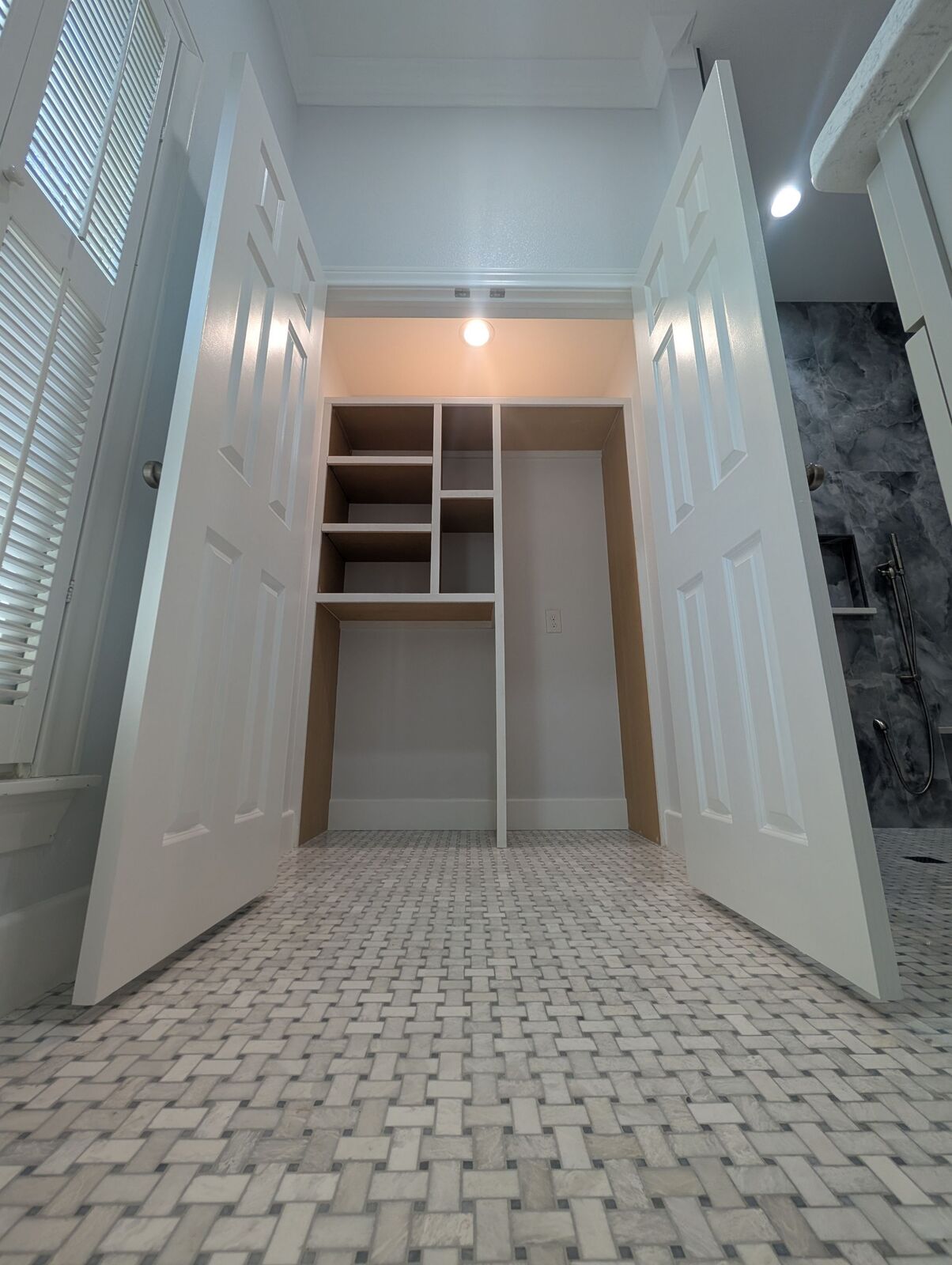 Bathroom closet with open double doors, built-in shelves and gray mosaic tile flooring.