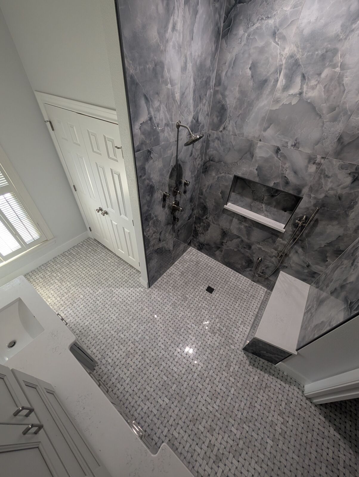 Large walk-in shower with gray marble-look tile, built-in niche, bench and patterned mosaic floor.