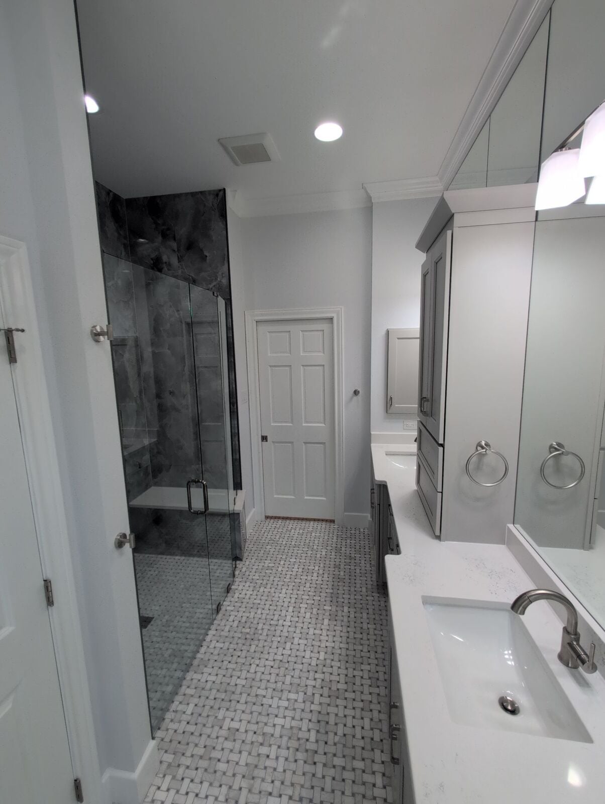 Remodeled bathroom with glass shower, gray vanity, white counter and bright mosaic tile floor.