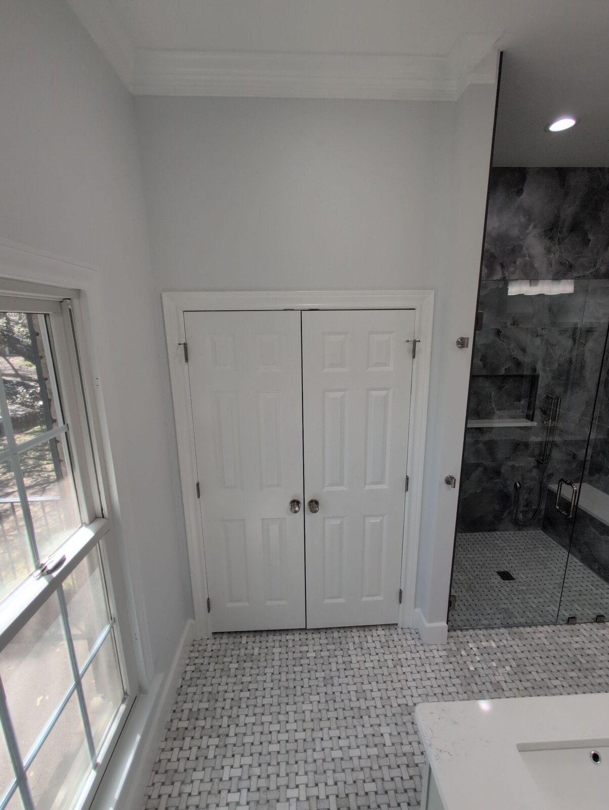 Updated bathroom with mosaic tile floor, white closet doors, window light and dark gray glass shower.