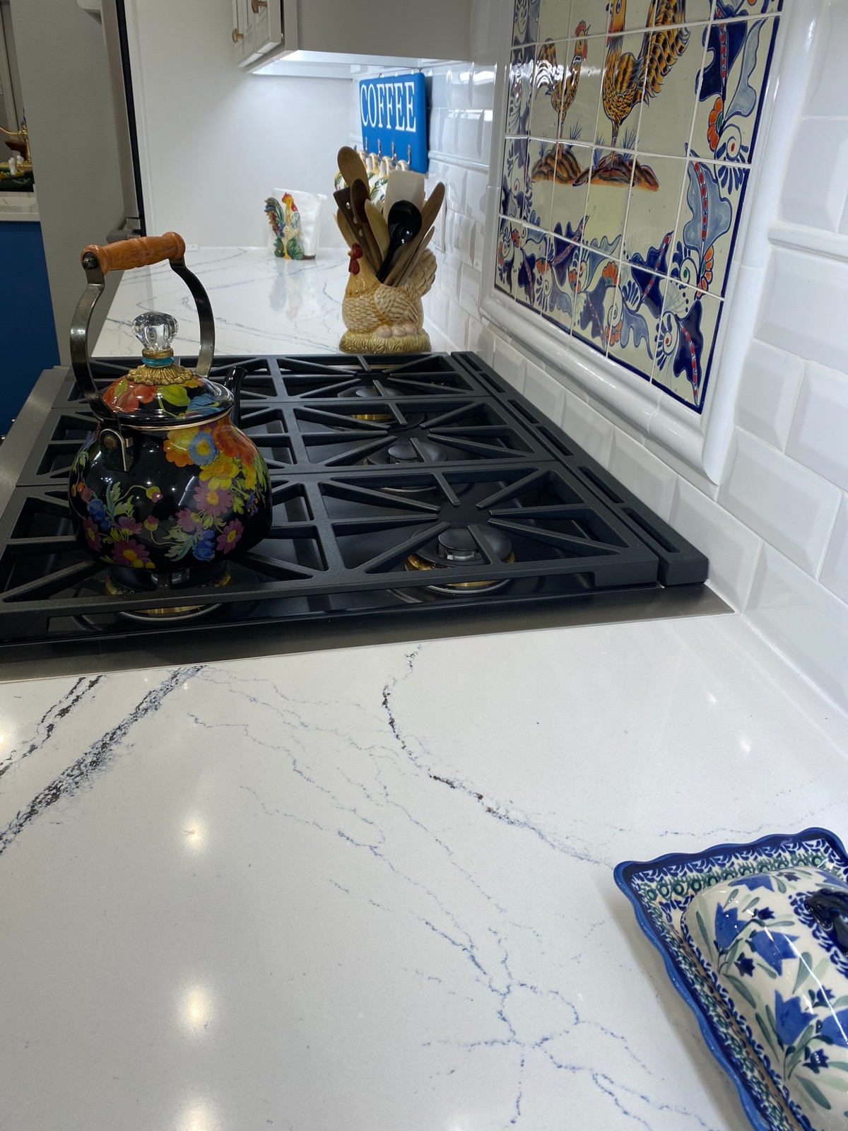 Gas cooktop and quartz counter beside colorful animal tile backsplash Gas cooktop and quartz counter beside colorful animal tile backsplash