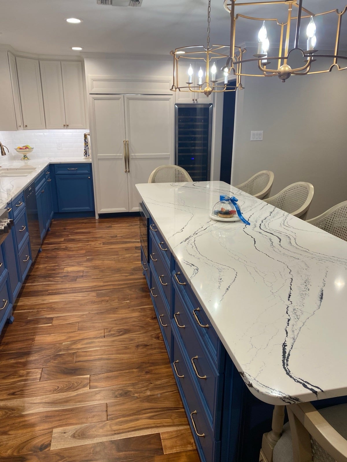 Navy kitchen with long quartz island, caned barstools and wood floor Navy kitchen with long quartz island, caned barstools and wood floor
